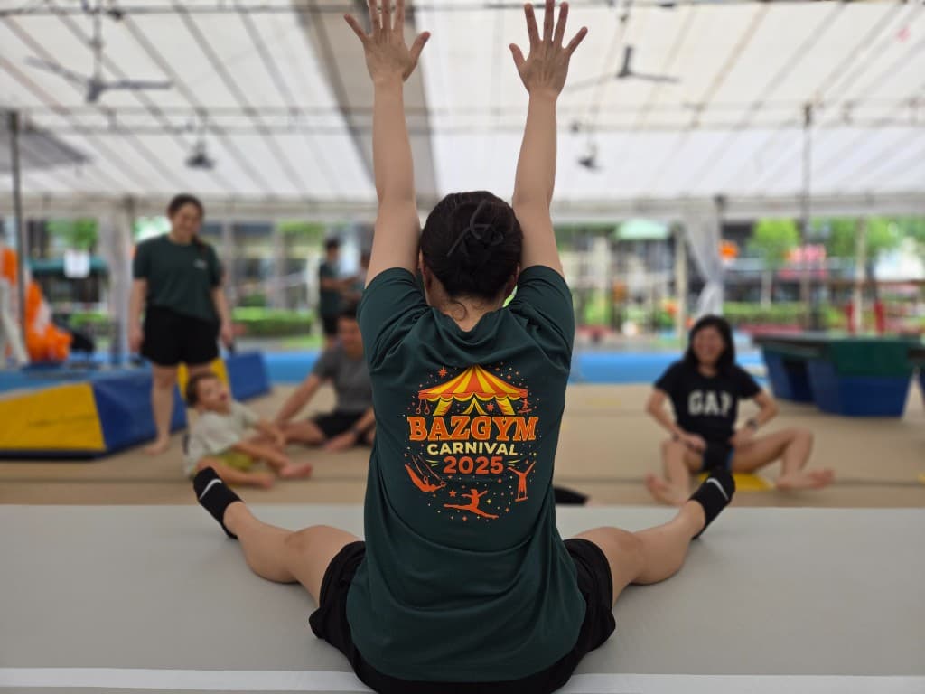 Participant at BazGym Carnival in a straddle stretch wearing the carnival shirt